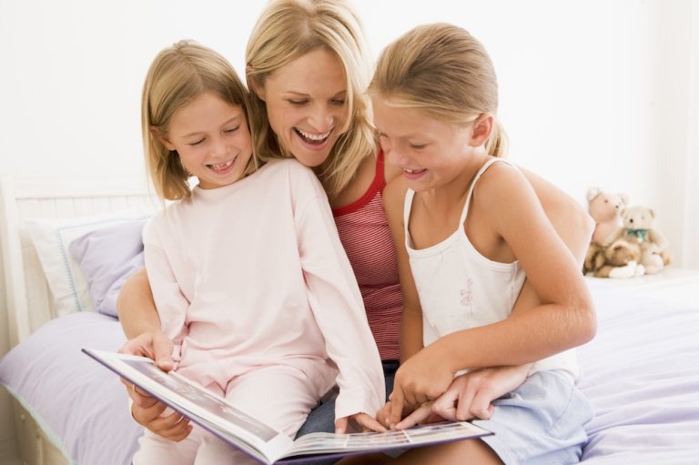 Mom reading books to two daughters.